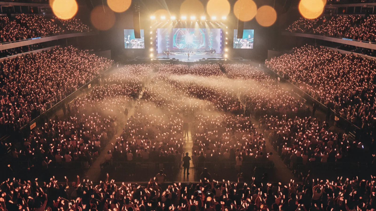 TWICE North American tour — pink and apricot lightsticks glowing across a packed arena crowd — KoreaHacks